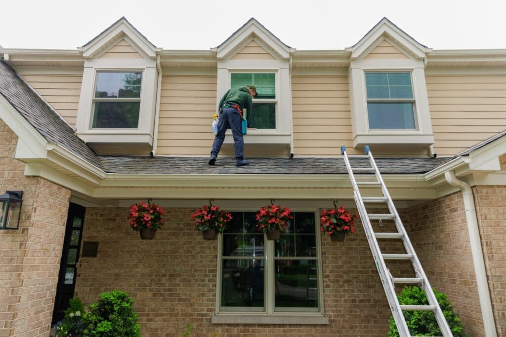 man window cleaning second floor windows by standing on the roof