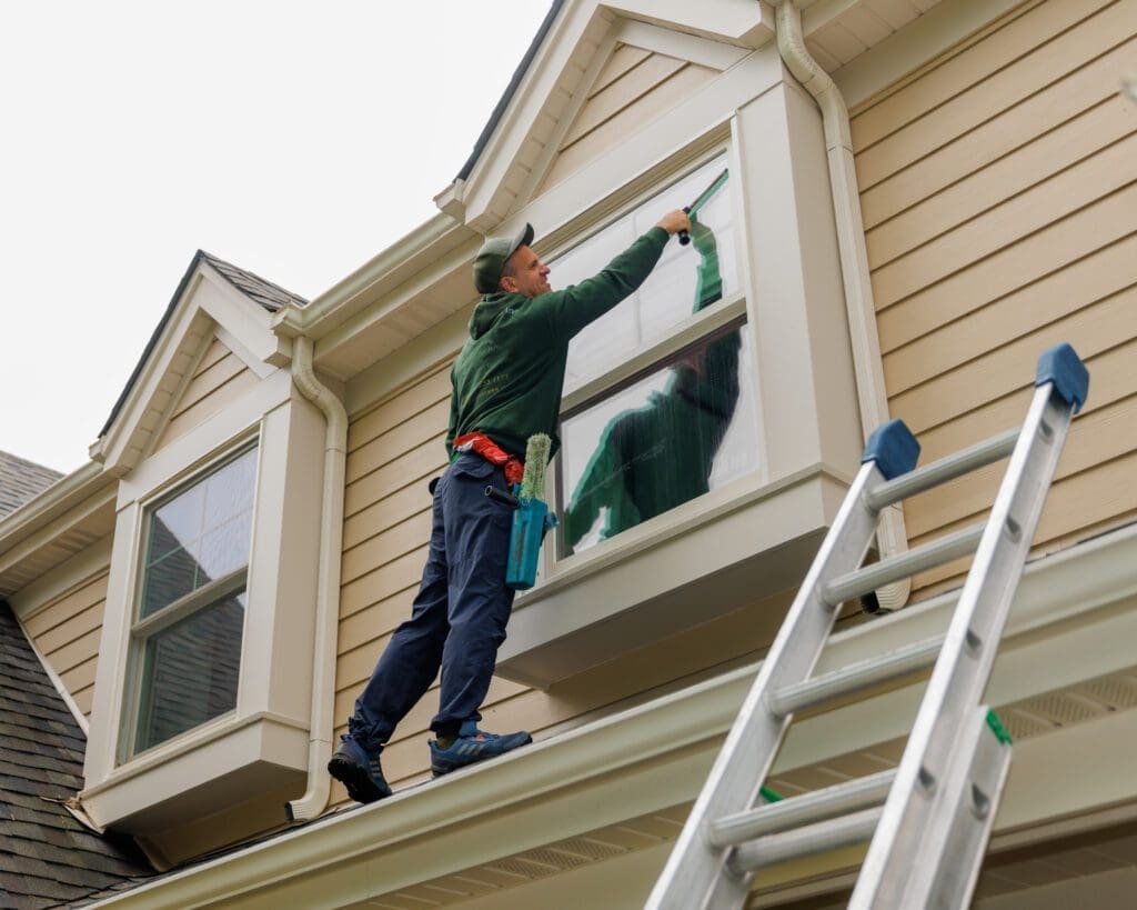 man cleaning a second story window with a squeegee