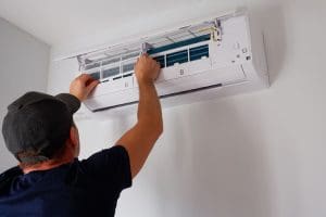 Maintenance of the air conditioner. A technician is cleaning the filter. View of the hands from the back.